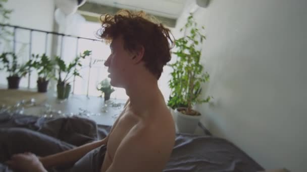 Young curly-haired guy falling down in bed and resting while having bad hangover in morning after party - Footage, Video