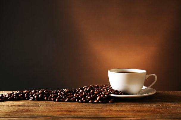 Šálek kávy s zrna na dřevěný stůl na tmavém pozadí - Fotografie, Obrázek
