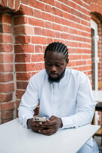 Afro-Amerikaanse man controleert mobiele telefoon in het café in de zomer dag. Millennial generatie en gen z mensen. Sociale netwerken en dating app - Foto, afbeelding