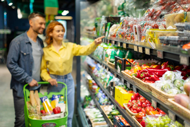 食料品ショッピング。 スーパーマーケットで食料品を選ぶ若いカップル,棚の新鮮な野菜に選択的な焦点 - 写真・画像