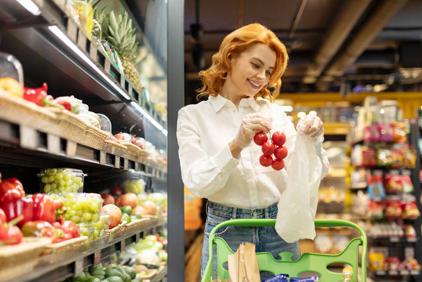 Eurooppalainen nainen valitsee tuoreita orgaanisia tomaatteja, ostaa vihanneksia ja tuotteita supermarketista. Kuluttajakäsite - Valokuva, kuva