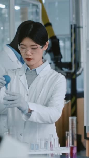 Medium vertical of Asian female researcher adding reagent to test tube, black male colleague with tablet approaching, sharing result of experiment, both discussing data - Footage, Video