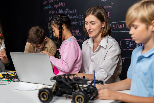 Lerarencodering om kinderen te laten zien hoe ze robots moeten coderen in de STEM-klasse. Kinderen leuk om te zien hoe leraar coderen met zelfverzekerde enige jongen in blauw shirt het nemen van nota met serieuze blik. Erutie. - Foto, afbeelding