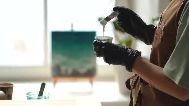 Pryskyřičné umění. Detailní záběr umělkyně hnětá míchání uměleckých epoxidových pryskyřic v plastovém kelímku, který pracuje v ateliérové dílně. Žena v ochranných rukavicích připravuje pryskyřici hnětením na požadovanou konzistenci. - Záběry, video