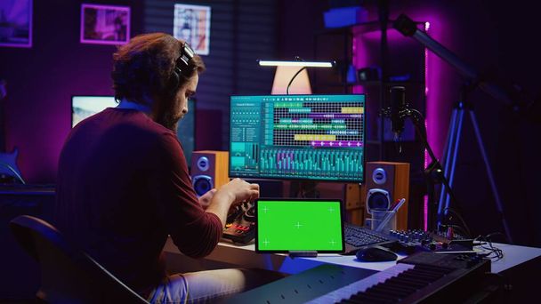 Ev stüdyosunda elektronik konsol ve ses panosuyla müzik karıştırma ve ustalaştırma sesleri modern melodiler yaratıyor. Ses mühendisi tablette yeşil ekranlı ses parçaları üretiyor. Kamera B. - Fotoğraf, Görsel