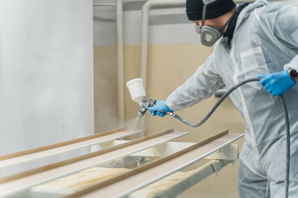 carpintero spray pintura pieza de madera mientras se trabaja en taller de carpintería. Foto de alta calidad - Foto, imagen