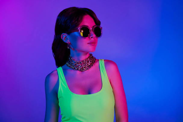 Foto di elegante ragazza clubber guardare da parte in top di occhiali da sole isolato sfondo a colori vivaci ultravioletti. - Foto, immagini