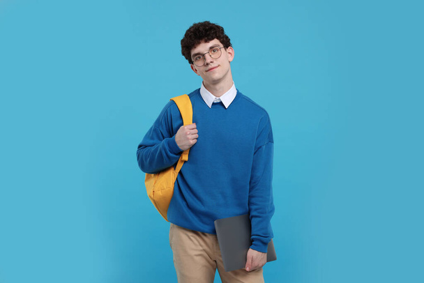 Portrait of student with backpack and laptop on light blue background - Fotoğraf, Görsel