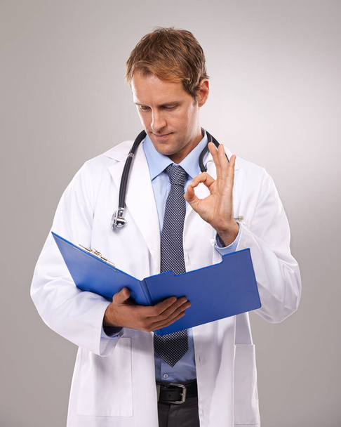 Clipboard, doctor and man in studio with okay sign for medical research, insurance and good news. Healthcare, hospital and worker with hand gesture for consulting, yes and planning on gray background. - Photo, Image