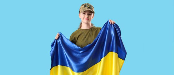 Młoda żołnierka z flagą Ukrainy na jasnoniebieskim tle  - Zdjęcie, obraz