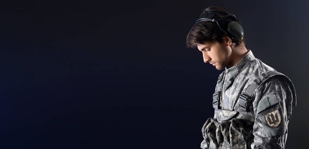 Joven soldado ucraniano sobre fondo oscuro con espacio para texto - Foto, Imagen
