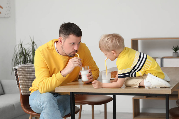 Маленький мальчик со своим отцом сидит за столом и пьет молоко в гостиной - Фото, изображение