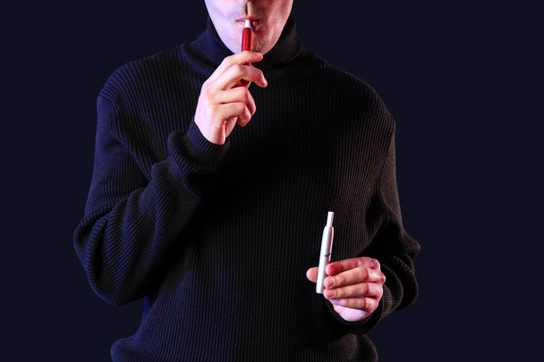 Νεαρός άνδρας καπνίζει ηλεκτρονικά τσιγάρα σε μαύρο φόντο - Φωτογραφία, εικόνα