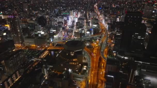 Leť nad nočním městem. Auta projíždějící víceúrovňovou křižovatkou v metropoli. Letecký pohled na městskou čtvrť v moderním městě. Ósaka, Japonsko, 20. ledna 2024 - Záběry, video