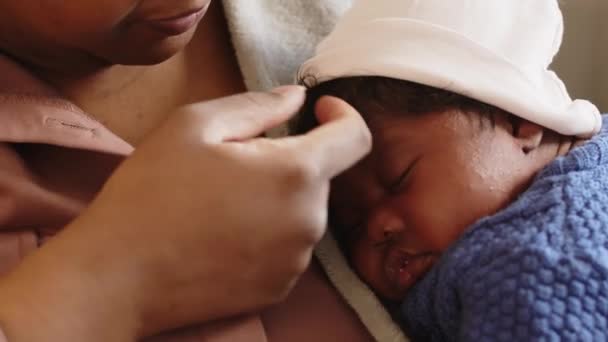 Closeup of young caring Black woman holding tiny sleeping baby in arms, adjusting white cap on baby head with tenderness - Footage, Video