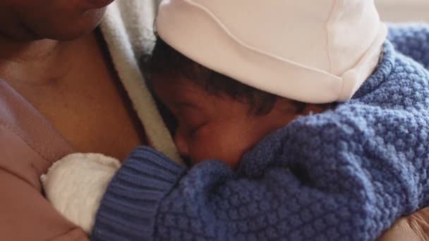 Close-up van slaperige Afro-Amerikaanse zuigeling baby dragen gezellige blauwe romper en witte krassen wanten wakker uit middagdutje in moeders armen - Video