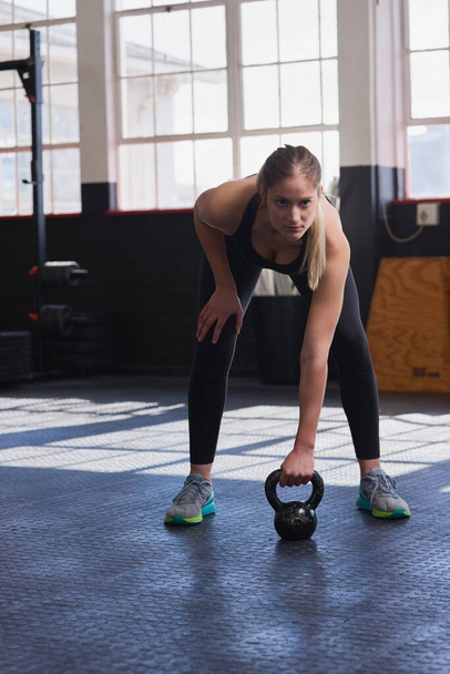Fitness, kettlebell and woman with motivation in gym for workout, training and strength for core muscle. Female athlete, physical activity or exercise with balance, endurance or commitment in sports. - Photo, Image