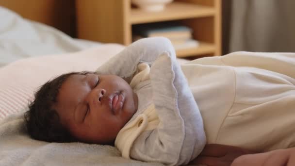kleine Afro-Amerikaanse baby meisje liggend op bed met haar ogen dicht wordt gekust door moeder zitten naast - Video
