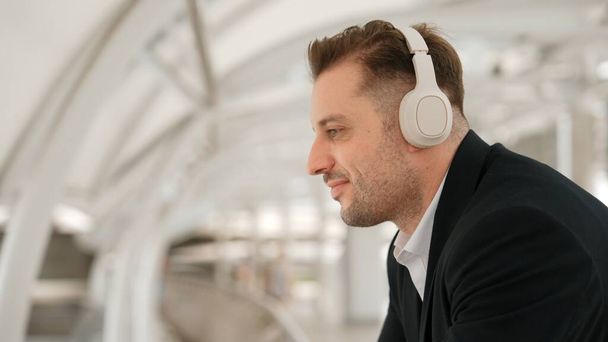 Close-up van de zakenman beweegt zijn hoofd naar muziek terwijl ontspannen luisteren lied van de hoofdtelefoon. Kaukasische manager draagt headset terwijl genieten van luisteren en bewegen gebaar en beweging in stedelijke stad Urbane. - Foto, afbeelding