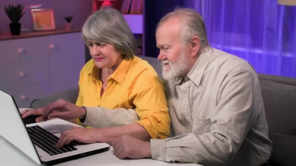modern entertainment voor gepensioneerden, oude man en oudere vrouw spelen computerspelletjes op laptop terwijl ze aan een tafel in de kamer zitten - Video