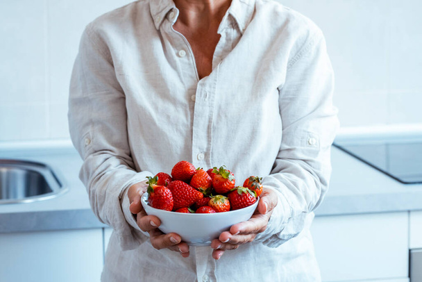  жінка показує червону полуницю з кухнею білого будинку на задньому плані. Люди і їжа здоровий спосіб життя натуральне харчування. Концепція калорій і схуднення - Фото, зображення