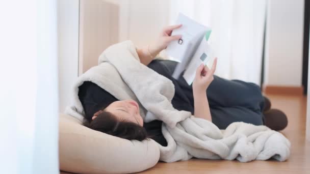 Концепція здоров'я та благополуччя з азіатською жінкою лягає і читає книгу у вітальні - Кадри, відео