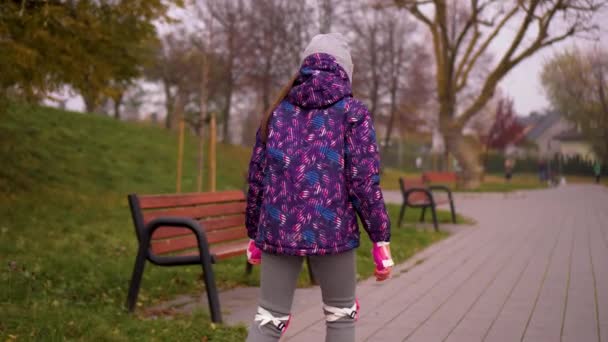 Κοριτσάκι στην άμυνα μαθαίνει πατινάζ σε πατίνια στο πάρκο της πόλης. Το παιδί απολαμβάνει το ενεργό άθλημα. Εκπαίδευση χόμπι ενεργό τρόπο ζωής αναψυχής παιδιά ξοδεύουν ελεύθερο χρόνο - Πλάνα, βίντεο