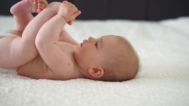 赤ん坊の女の子は白いシートに横たわり,足を握っています - 映像、動画