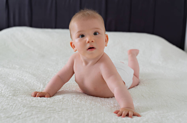 おむつにかわいい6ヶ月の赤ちゃんが白い毛布の上に胃の上に横たわっています - 写真・画像