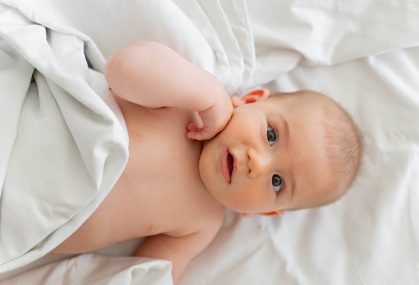 Altında bez olan bebek beyaz bir battaniyeyle sırt üstü yatıyor. - Fotoğraf, Görsel