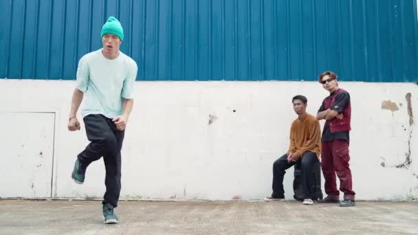 Jovem dançarina de rua dançando em estilo hip hop com amigos multiculturais torcendo atrás na parede. Bonito homem atraente esticar os braços na rua com fundo azul. Desporto ao ar livre 2024. hiphop. - Filmagem, Vídeo
