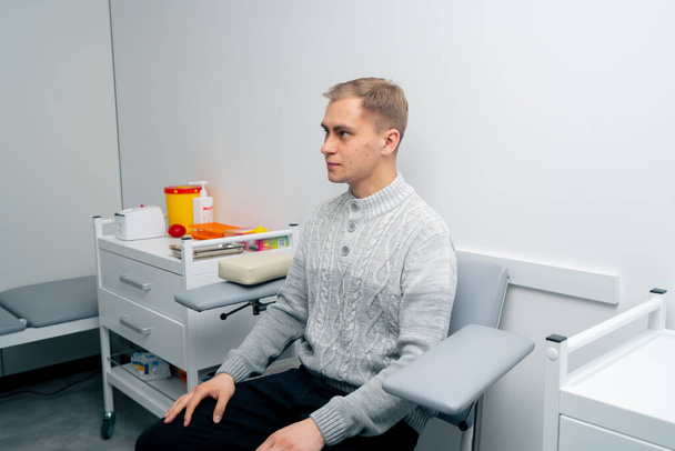 em uma clínica privada no escritório um paciente um cara jovem senta-se antes de fazer testes - Foto, Imagem