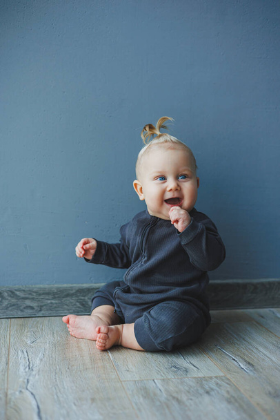 Un niño de 7 meses con una cola en la cabeza. El bebé está sentado en el suelo y sonriendo. - Foto, Imagen