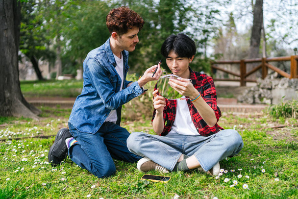 casal LGBT goza de um tutorial de maquiagem juntos em um parque sereno. - Foto, Imagem