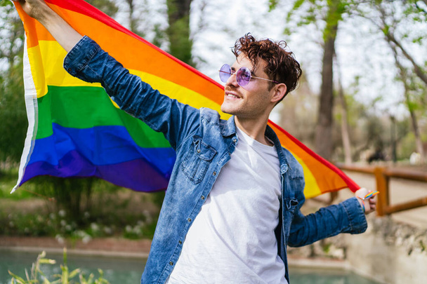 Un homme gay heureux agite le drapeau LGBT coloré, célébrant la diversité et la fierté à l'extérieur. - Photo, image