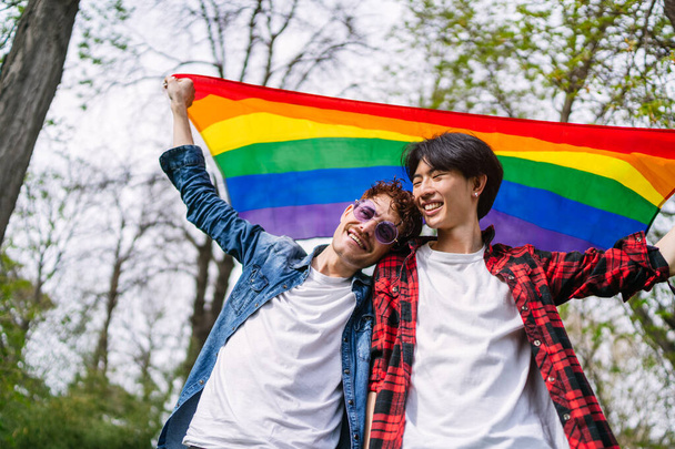 Китайская гей-пара счастливо держит яркий ЛГБТ-флаг на открытом воздухе, демонстрируя любовь и гордость. - Фото, изображение