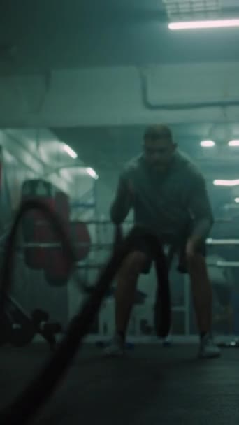 Αθλητικός άνθρωπος ασκήσεις με σχοινιά μάχης στο σκοτεινό γυμναστήριο πυγμαχίας. Επαγγελματική αρσενικό πυγμάχος κάνει καρδιο ή προπόνηση αντοχής πριν από τον αγώνα πρωτάθλημα. Σωματική δραστηριότητα Κάθετη βολή - Πλάνα, βίντεο