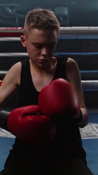 Vertikální výstřel Teenager sedí blízko boxerského ringu a nasazuje si boxerské rukavice. Mladý boxer přichází v boxerském ringu a začíná cvičit punče s afroamerickým trenérem. Sportovec se připravuje na soutěž v - Záběry, video