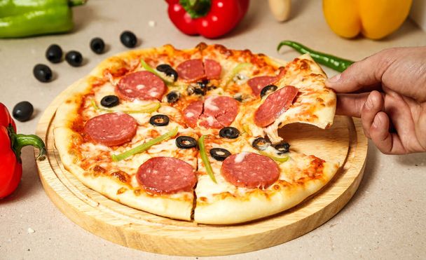 Een persoon gebruikt vakkundig een mes om een peperoni pizza in plakjes te snijden op een houten snijplank.. - Foto, afbeelding