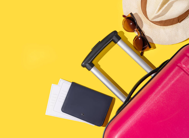 Plochý růžový kufr s cestovním příslušenstvím, kloboukem a slunečními brýlemi na žlutém pozadí. Cestovní koncept. Horní pohled a místo pro kopírování. - Fotografie, Obrázek