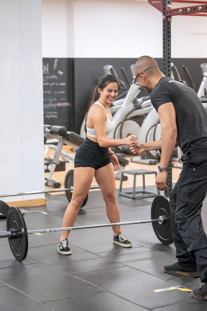 Een vrolijke vrouw bereidt zich voor op een gewichtheffen sessie, het delen van een moment met haar personal trainer in een fitnessruimte.  - Foto, afbeelding
