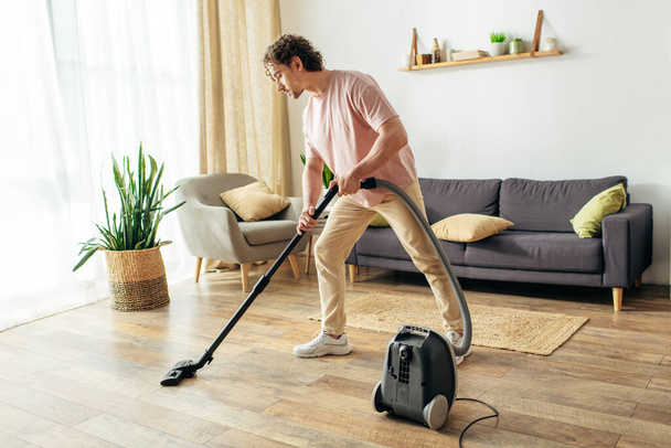 Ein gutaussehender Mann in kuscheliger Hauskleidung saugt akribisch ein Wohnzimmer. - Foto, Bild