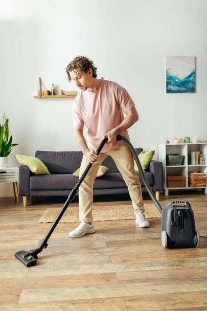 Man in gezellige huiskleding maakt gebruik van vacuüm te reinigen vloer. - Foto, afbeelding