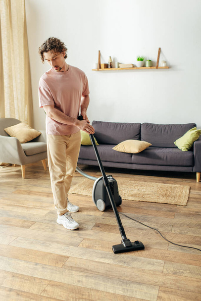 Een man in knusse huiskledij stofzuigt de woonkamer vloer. - Foto, afbeelding