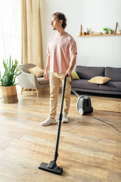 Handsome man in cozy homewear vacuuming on hardwood floor. - Photo, Image