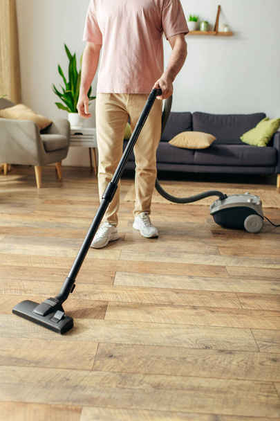 Un uomo in accogliente biancheria da casa utilizza un aspirapolvere per pulire un pavimento in legno. - Foto, immagini