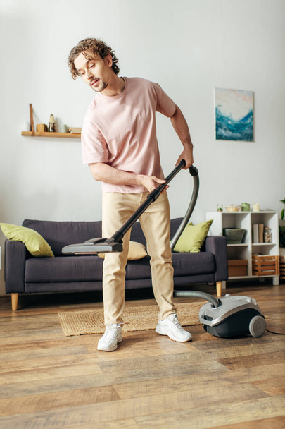 Ein gutaussehender Mann in kuscheliger Hauskleidung saugt fleißig sein Wohnzimmer. - Foto, Bild