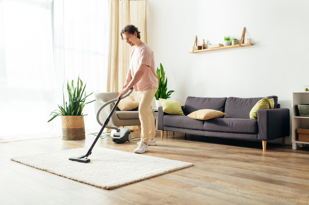 Um homem bonito em homewear acolhedor limpa sua casa usando um aspirador de pó. - Foto, Imagem