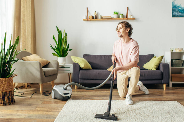 A man in cozy homewear diligently vacuums a living room. - Photo, Image