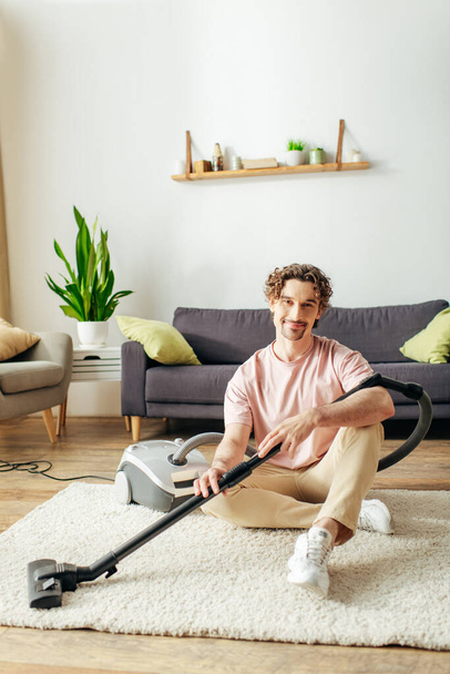Knappe man in gezellige huishoudkleding schoonmaken met een vacuüm op de vloer. - Foto, afbeelding